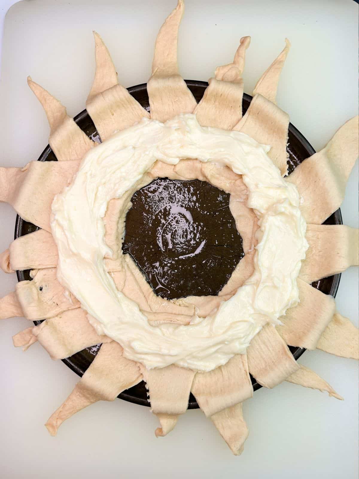sweetened cream cheese on top of crescent roll triangles in circle shape.