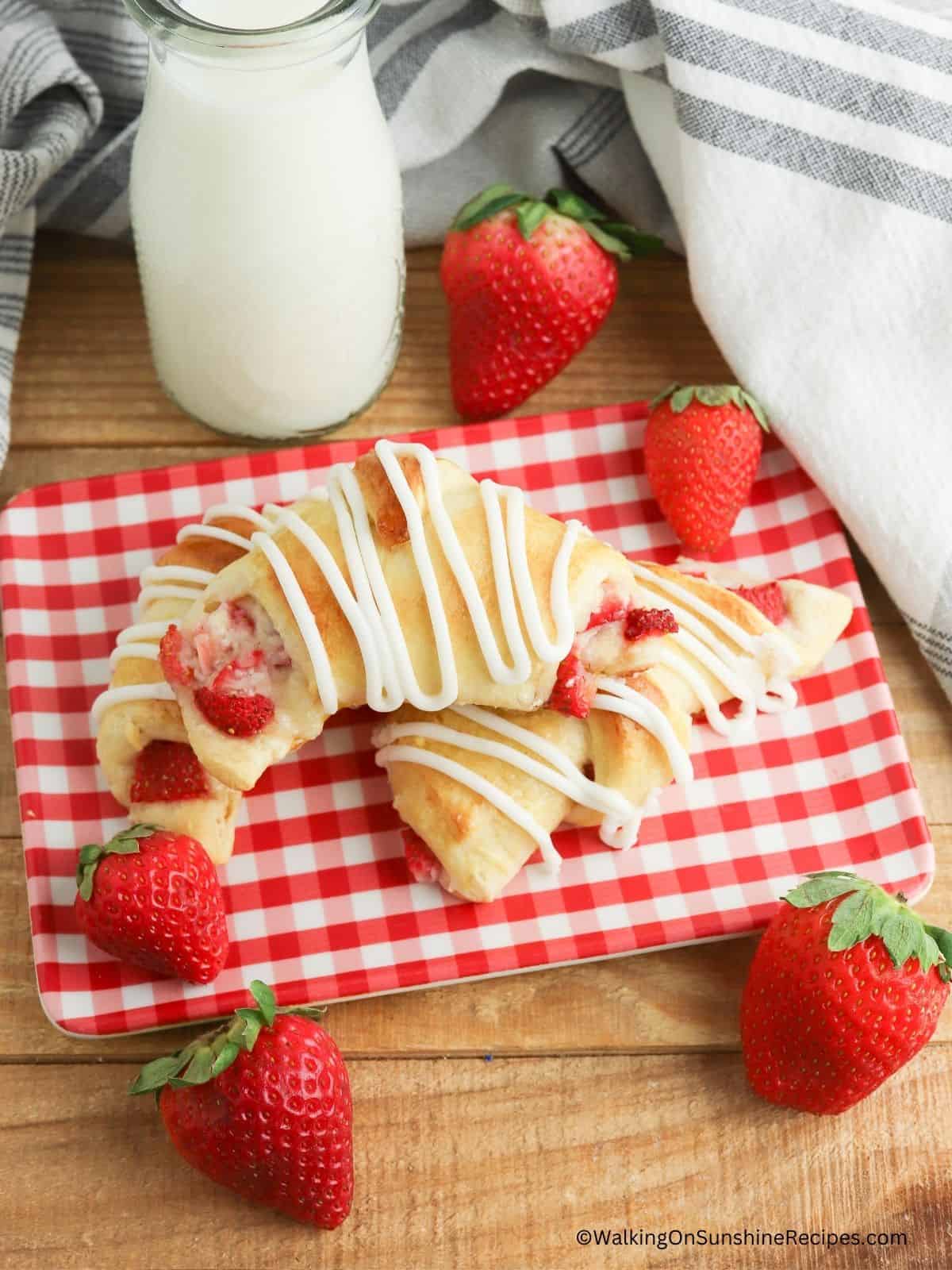 Crescent rolls on red checked plate with fresh strawberries.