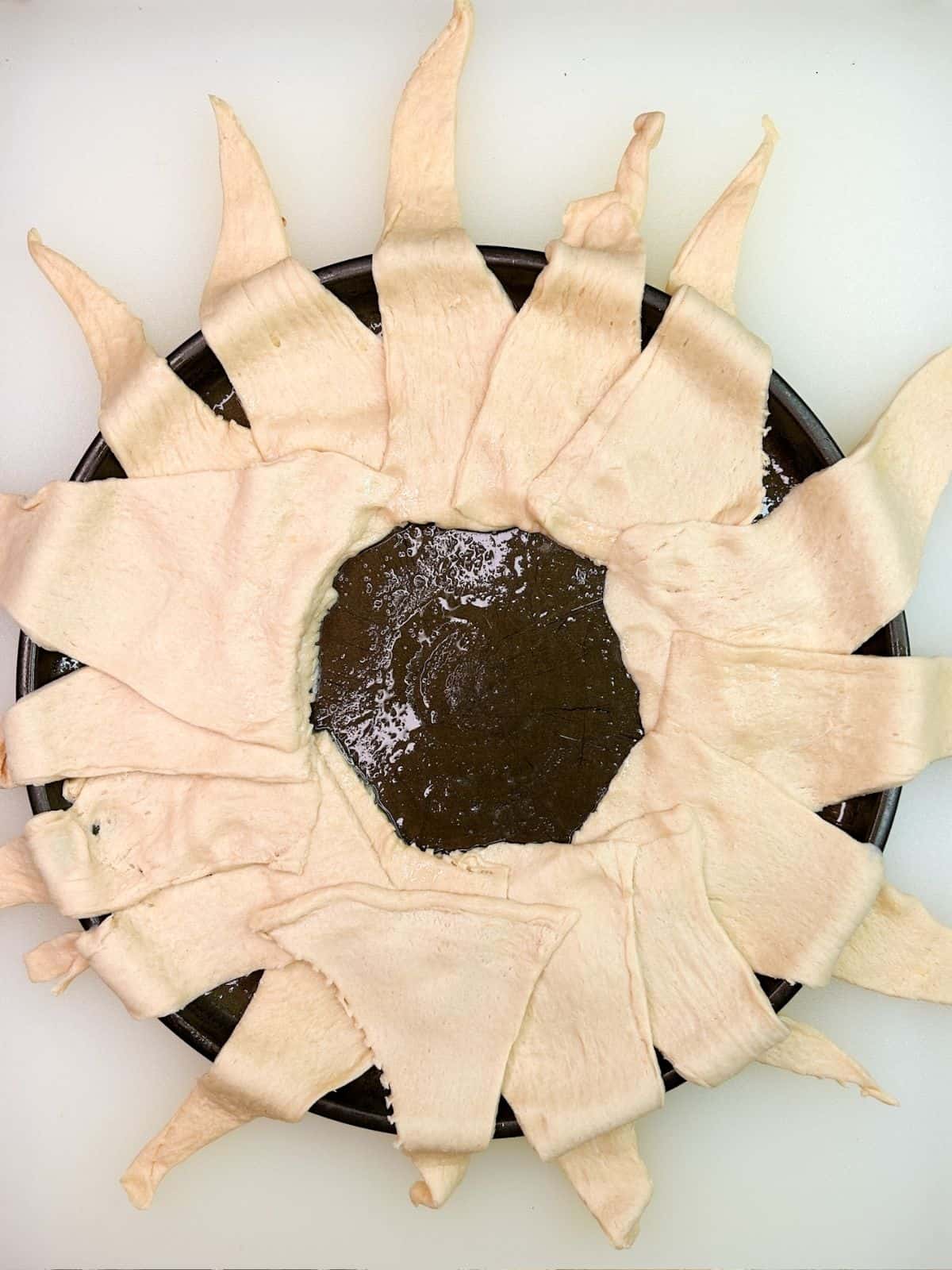 Lay crescent roll triangles in circle on top of round baking tray.