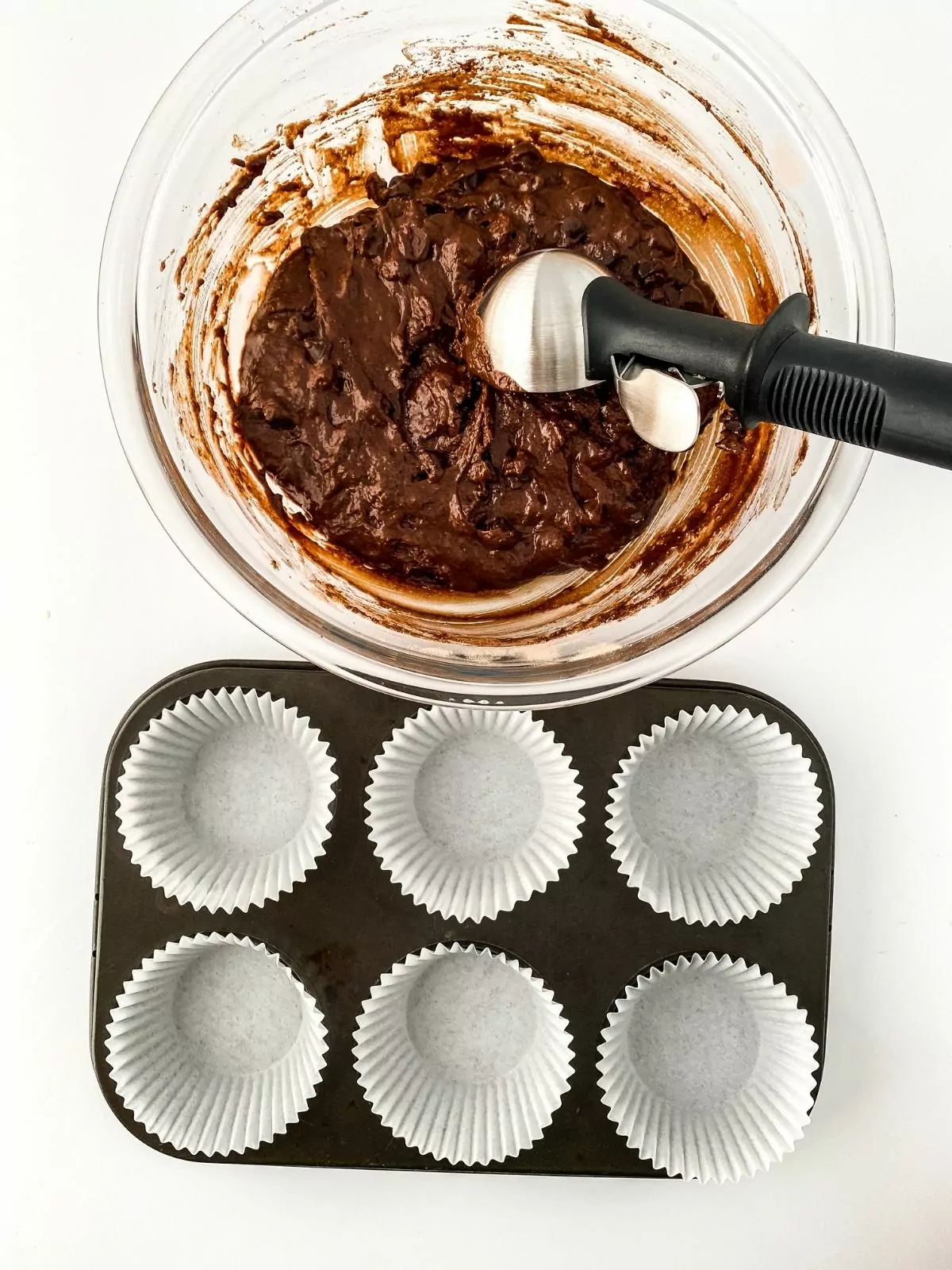 add muffin mix to paper liners in muffin pan using cookie scoop.