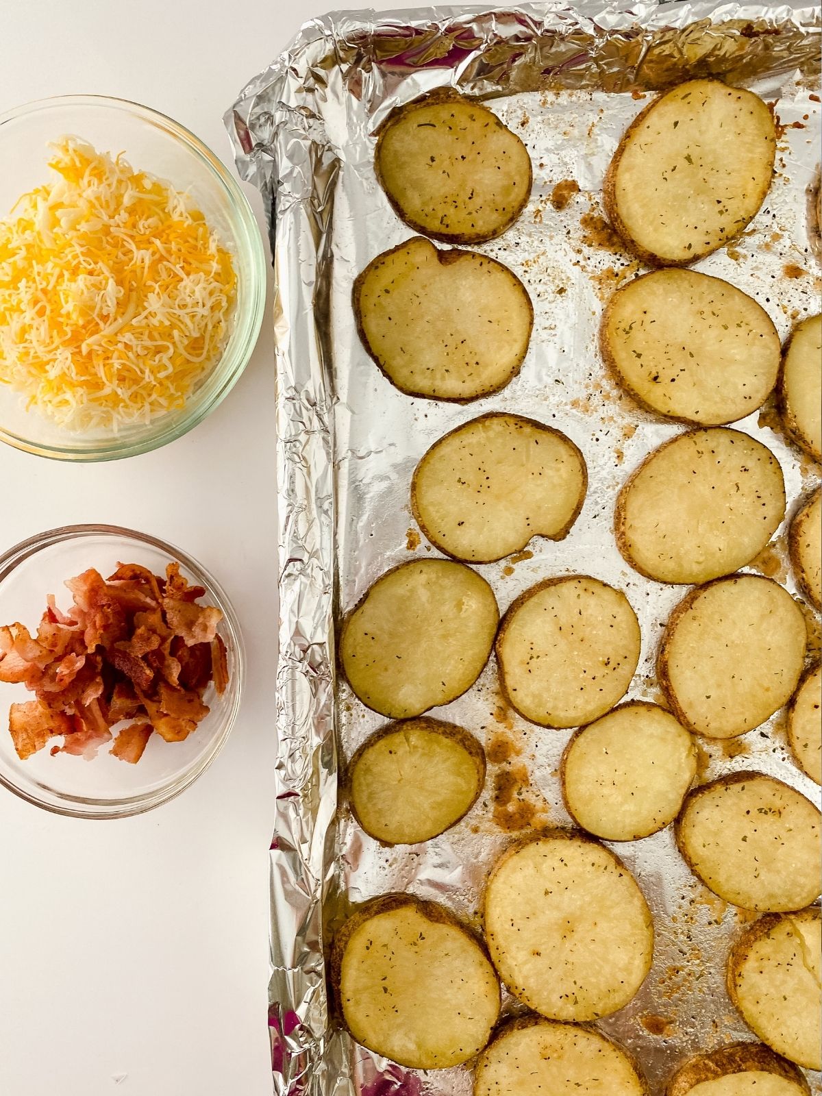 baked potato slices on baking tray with bowl of bacon and cheese.