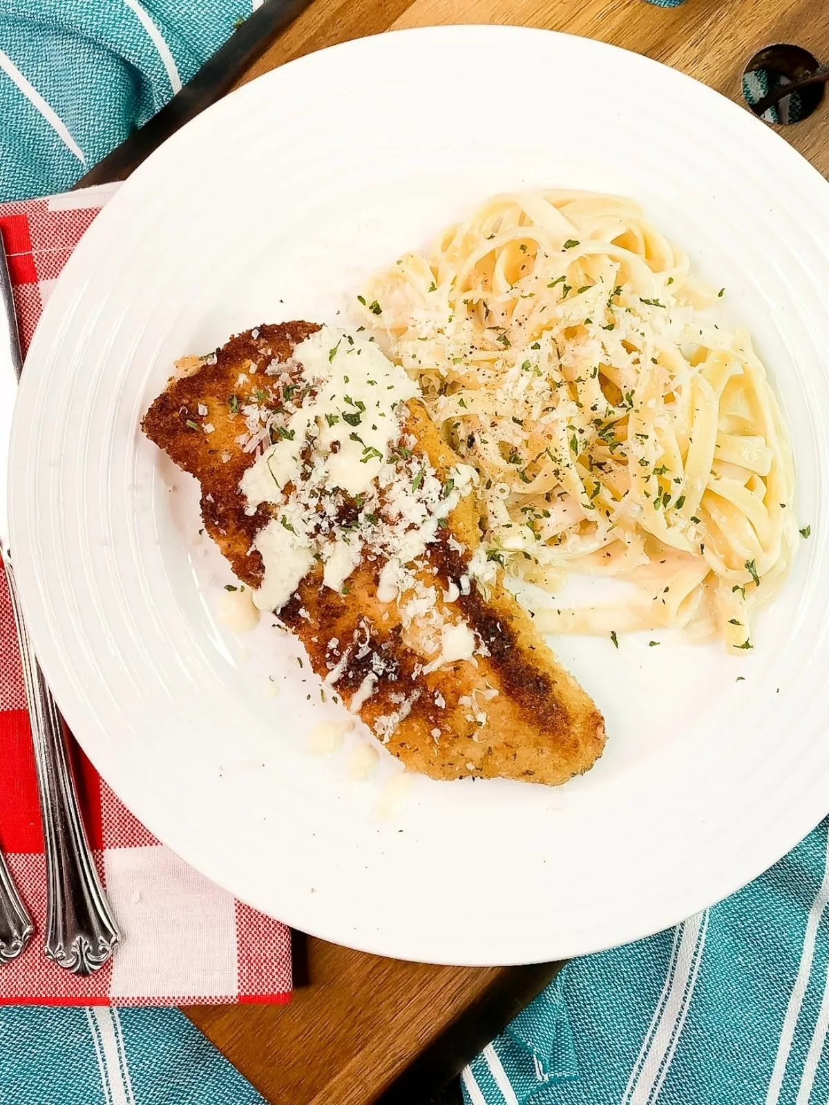 Chicken Cutlets Parmesan Recipe with pasta and Alfredo sauce on plate with fork and knife.
