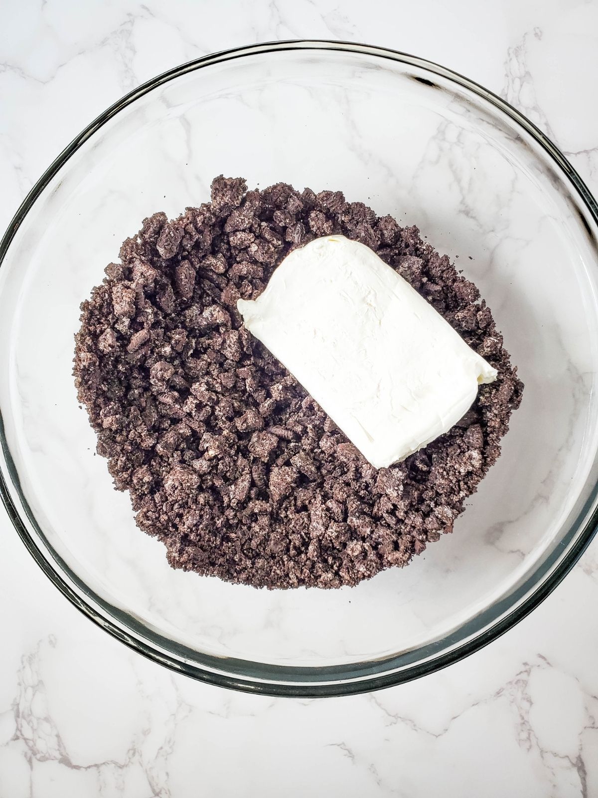 Crushed Oreo cookies with block of cream cheese in bowl.