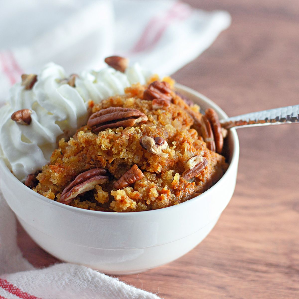 White bowl filled with pumpkin cobbler and whipped cream.