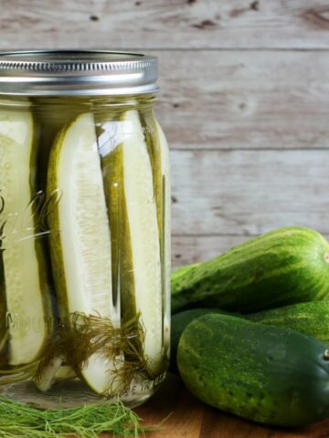 Pickles in jar with cucumbers on cutting board.