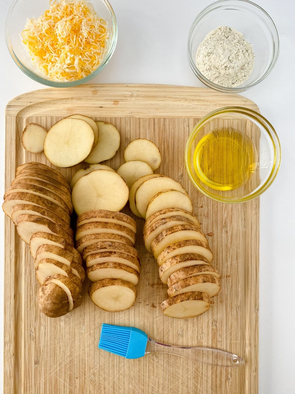 Sliced potatoes on cutting board with cheese, and seasoning mix.