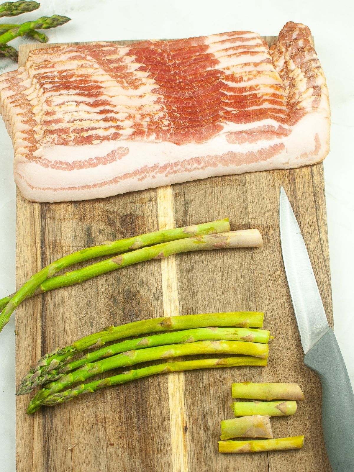 ends cut off of asparagus on cutting board with slices of bacon.