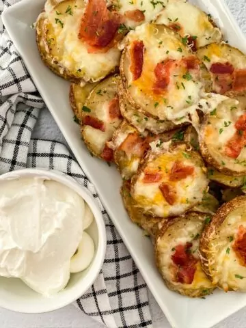 baked potato slices on white tray with cheese and bacon, sour cream in small bowl on the side.