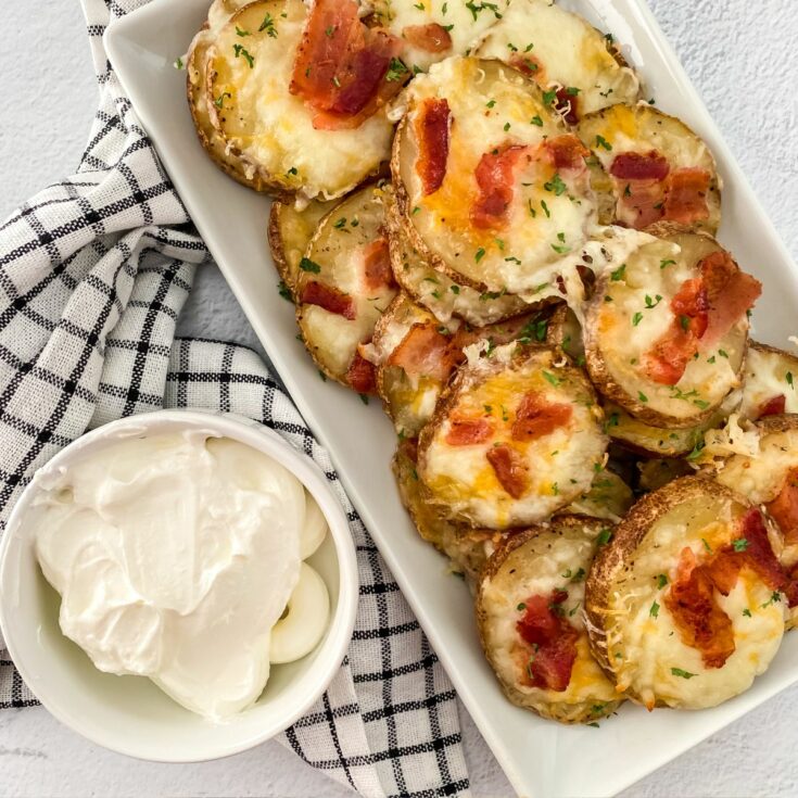 baked potato slices on white tray with cheese and bacon, sour cream in small bowl on the side.
