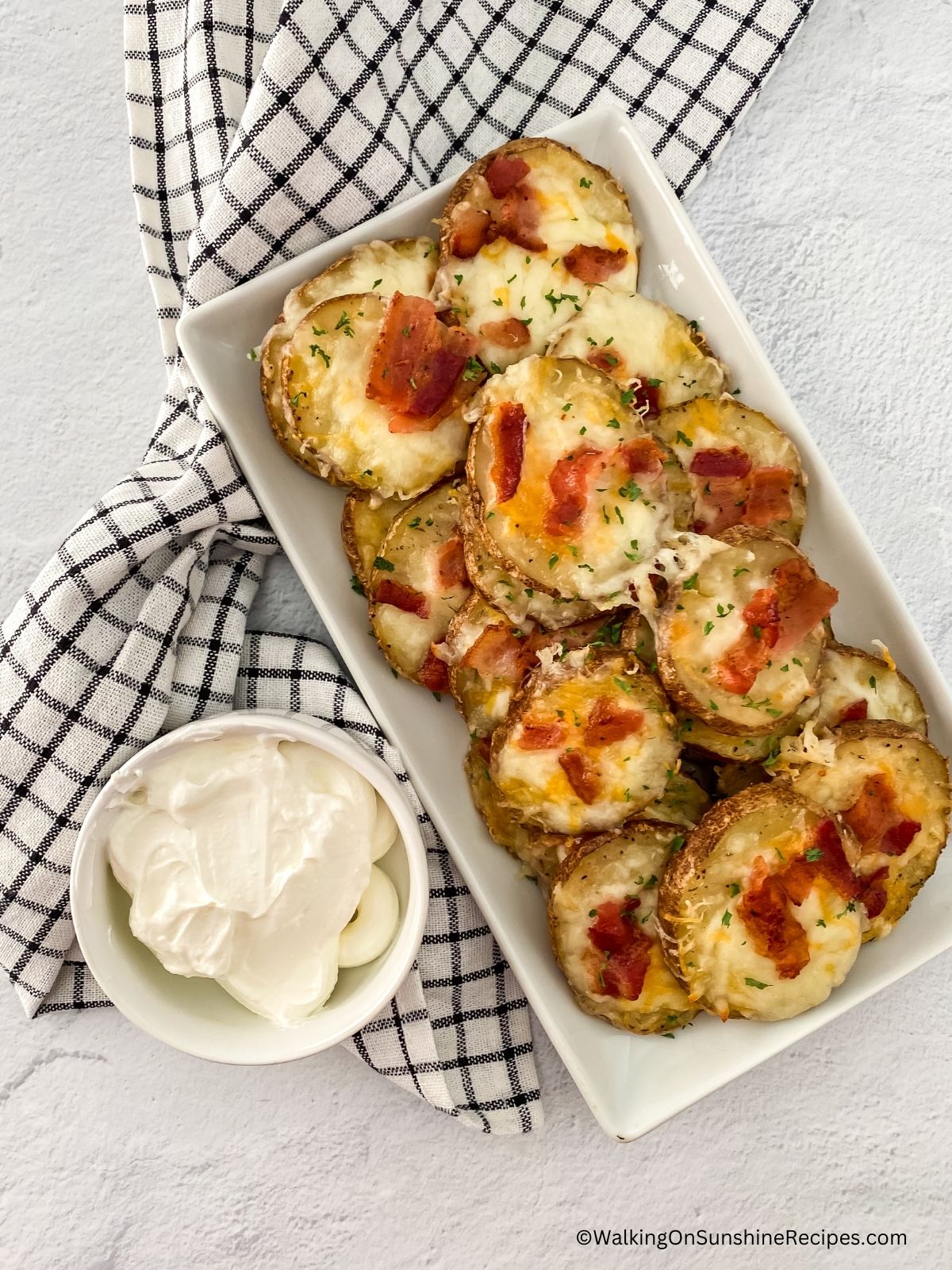 Bacon cheese potatoes on white tray with sour cream in small bowl.