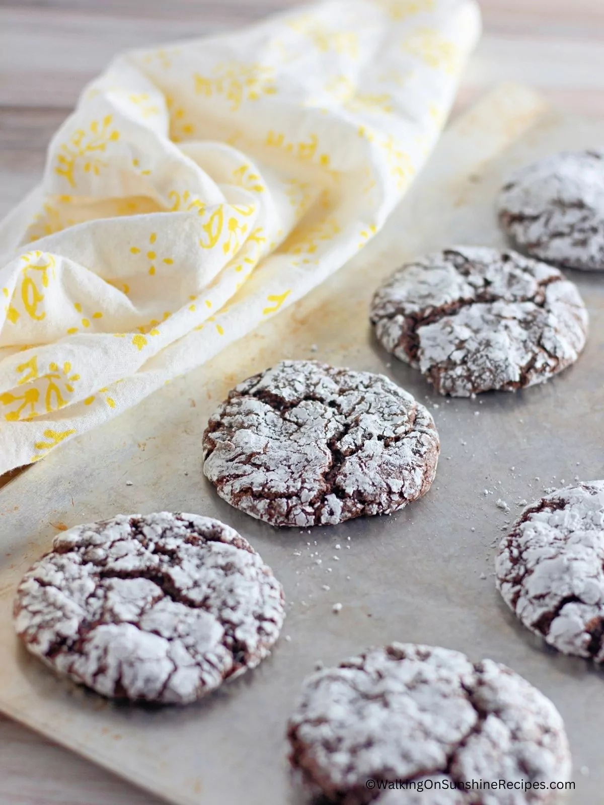 Chocolate cake mix cookies on baking tray with yellow dish towel.