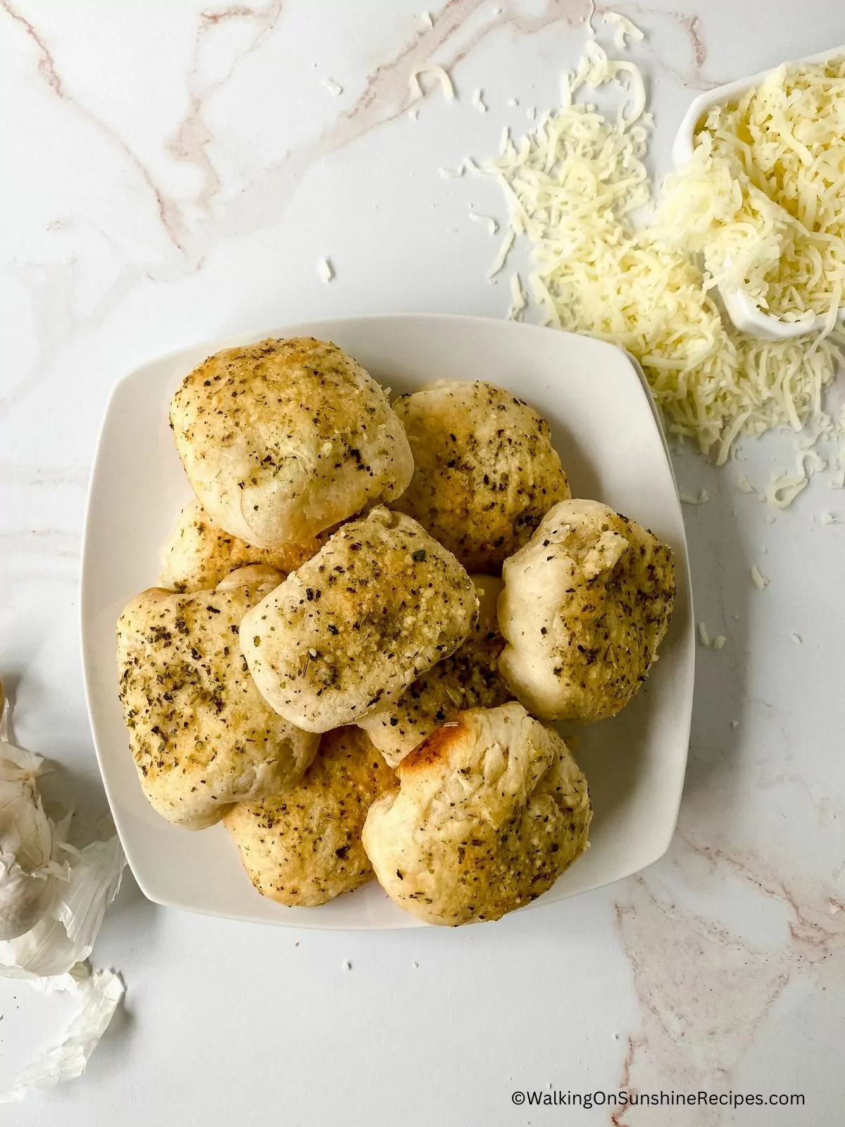 Baked biscuits on white plate with garlic bulbs and Parmesan cheese.