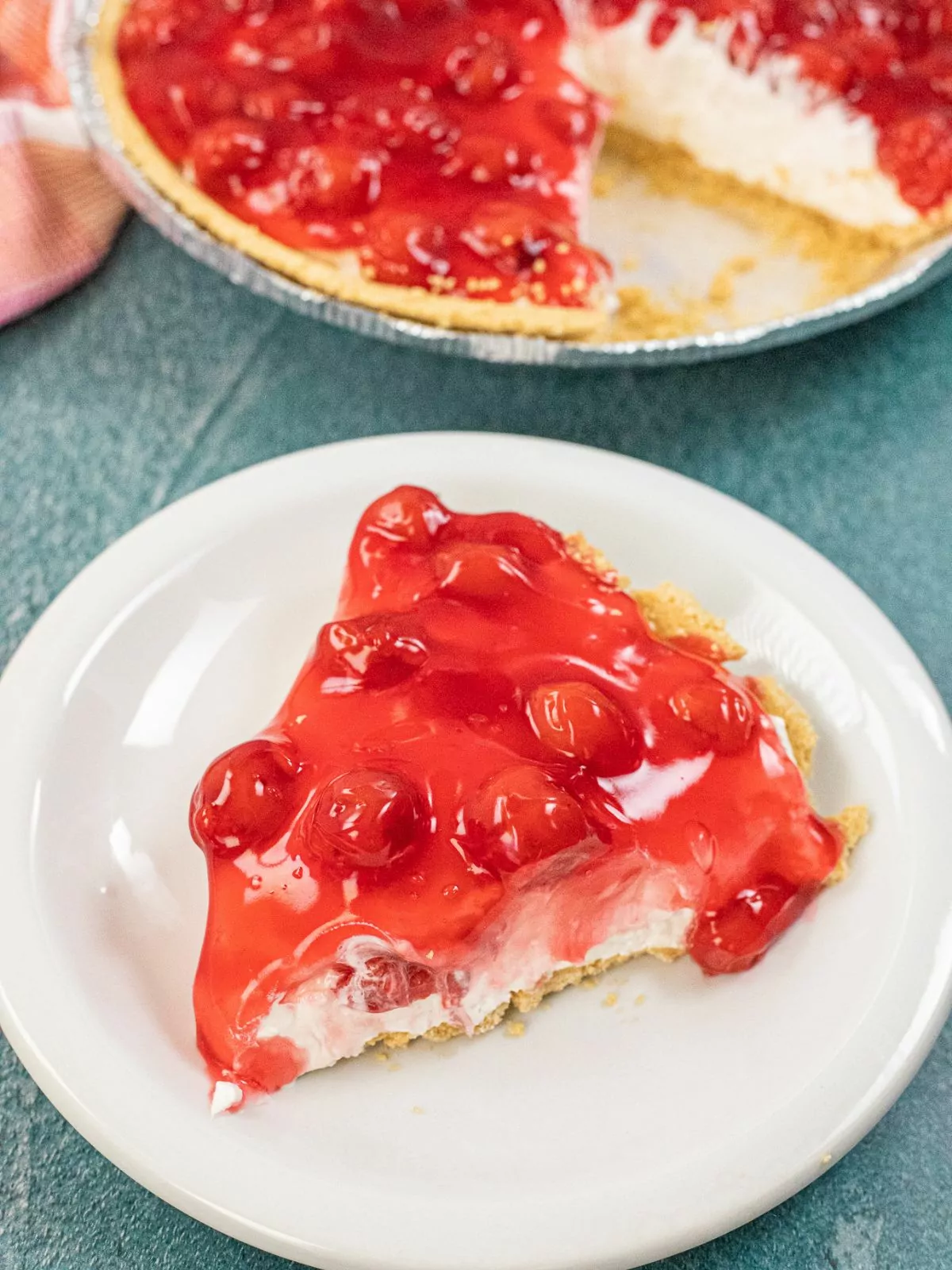 slice no bake cheesecake pie on white plate with cherrypie filling.