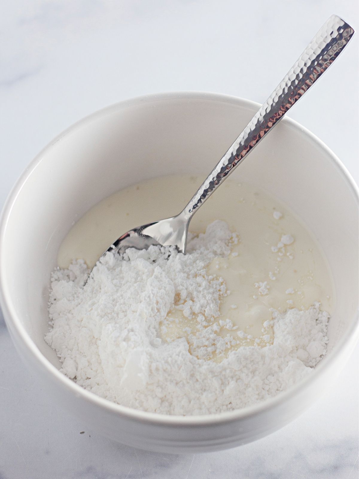 Powdered sugar glaze in white bowl with spoon.