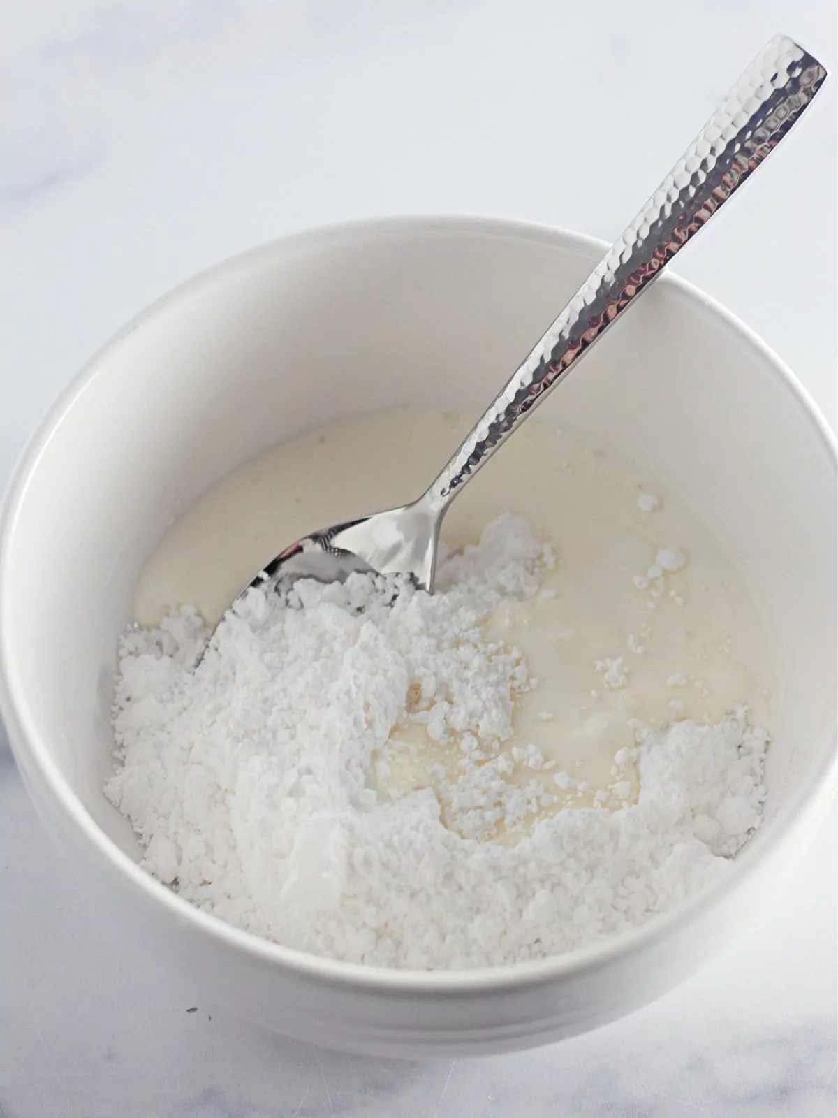Powdered sugar glaze in white bowl with spoon.