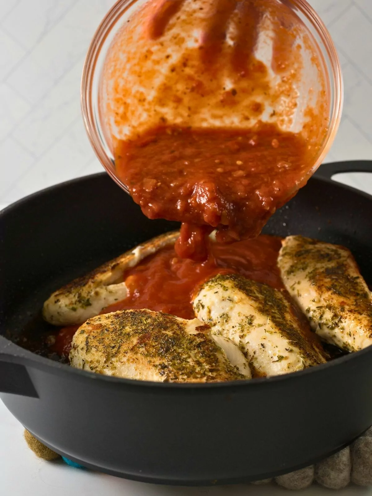 Add tomato sauce on top of browned chicken breasts in cast iron skillet.