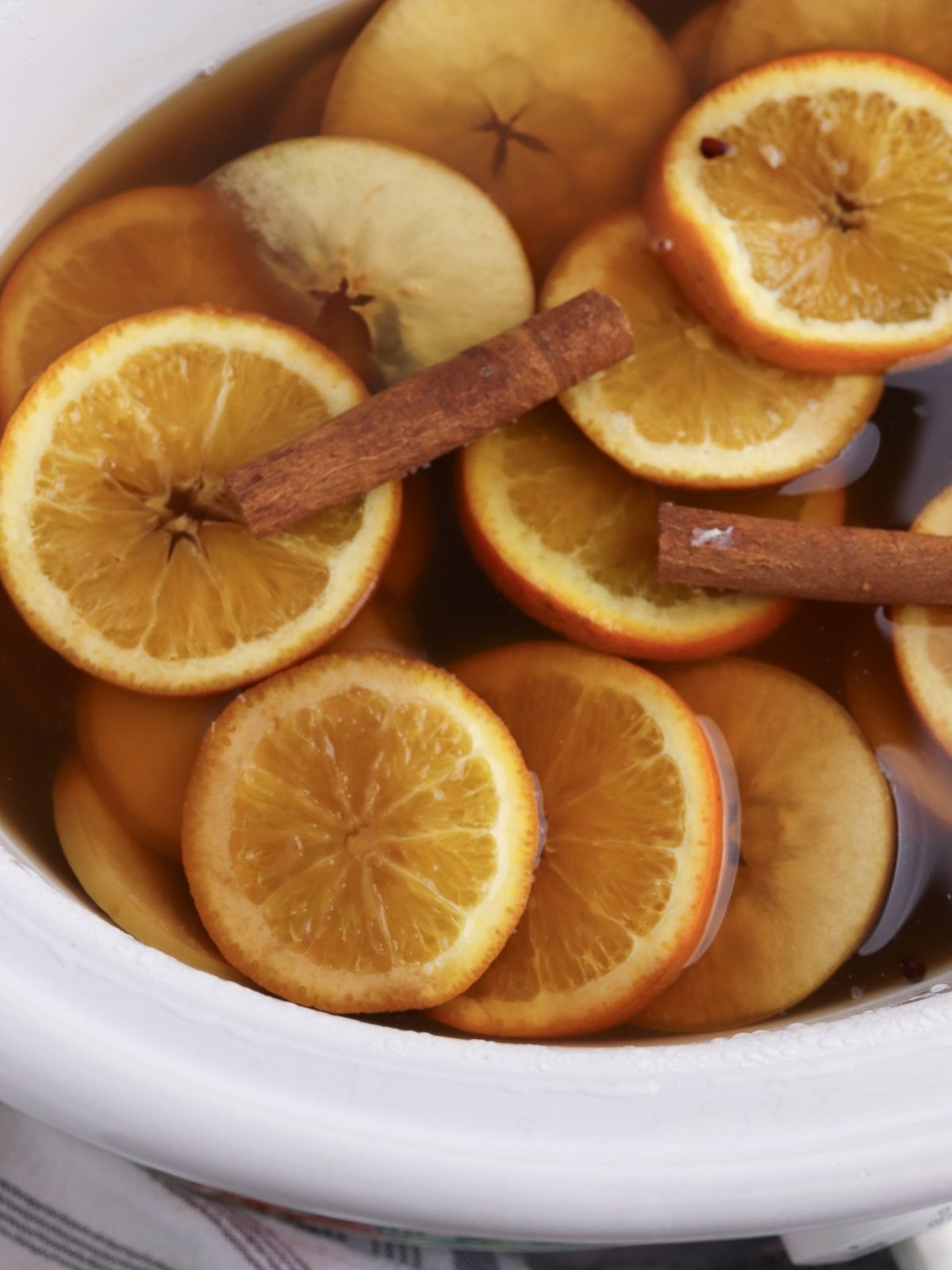 slow cooker cider with apple and orange slices with cinnamon sticks.