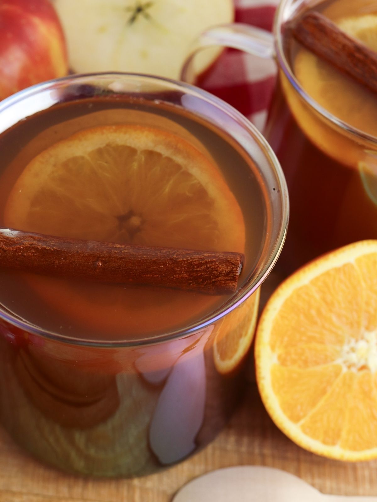 apple cider served in glasses with oranges, apples and cinnamon sticks.
