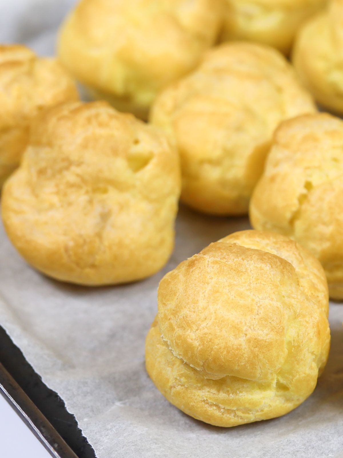 Baked cream puffs on tray with parchment paper.