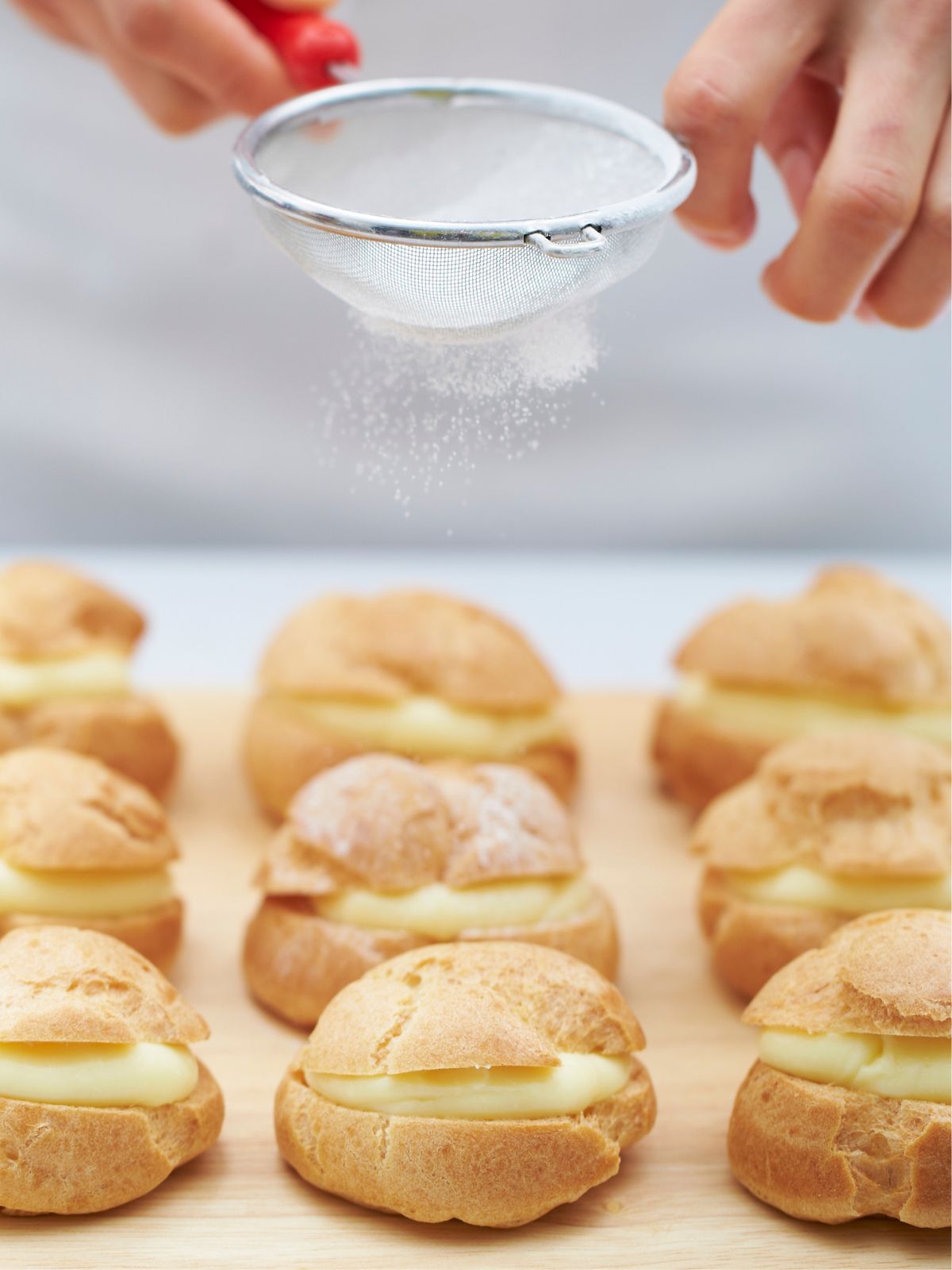 sprinkling powdered sugar on top of cream puffs with vanilla pudding.