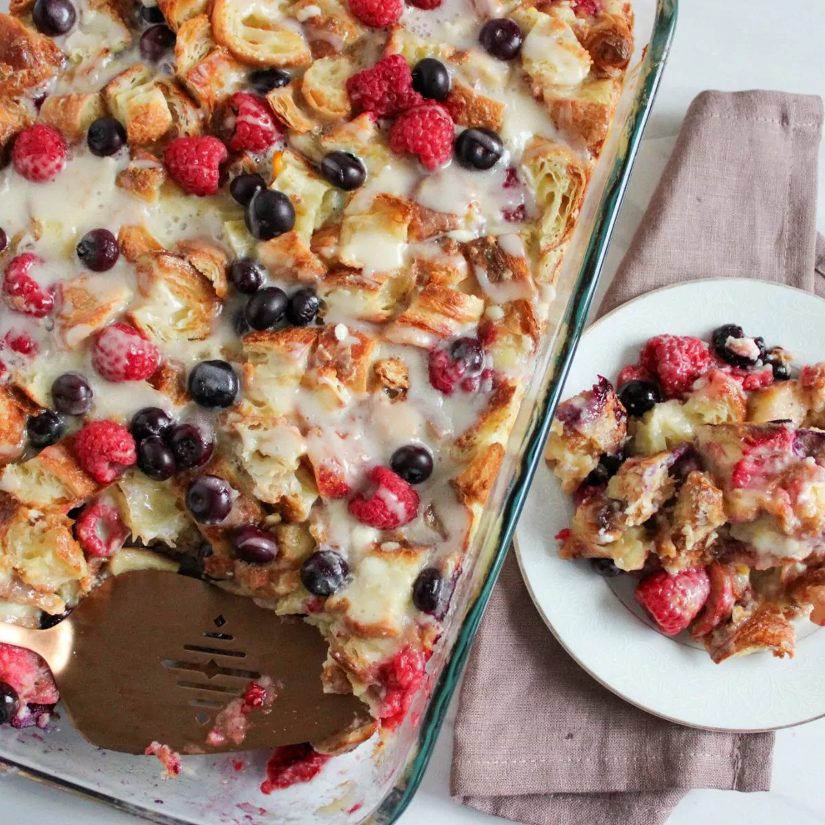 scoop of berry breakfast casserole on a white plate next to the casserole dish.