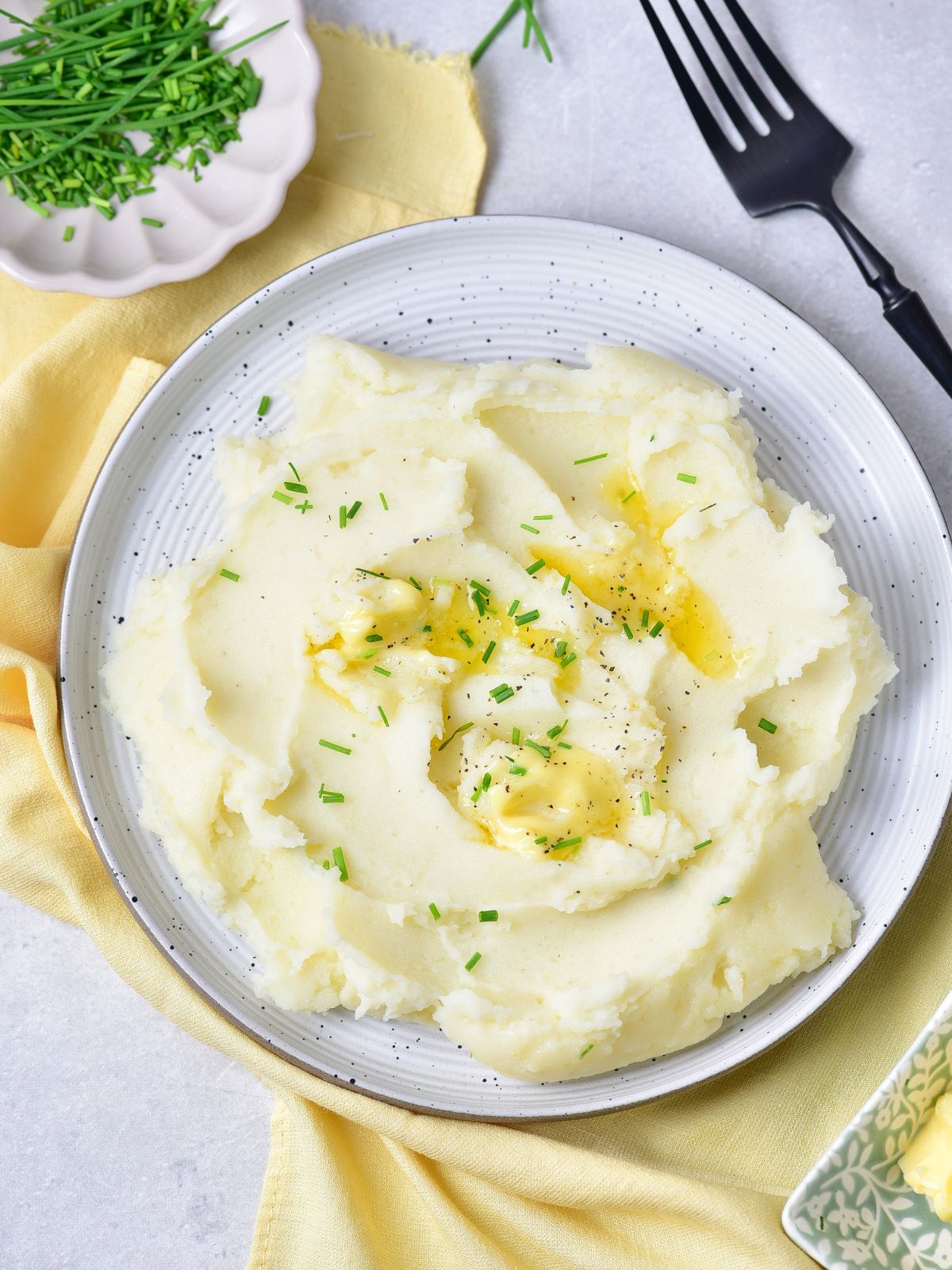 mashed potatoes on plate with small plate of chopped herbs.