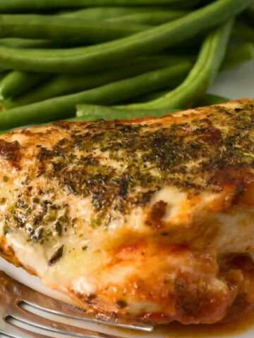 A baked chicken breast with green beans on the side.