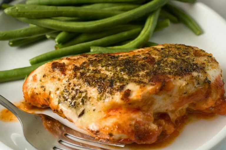 A baked chicken breast with green beans on the side.