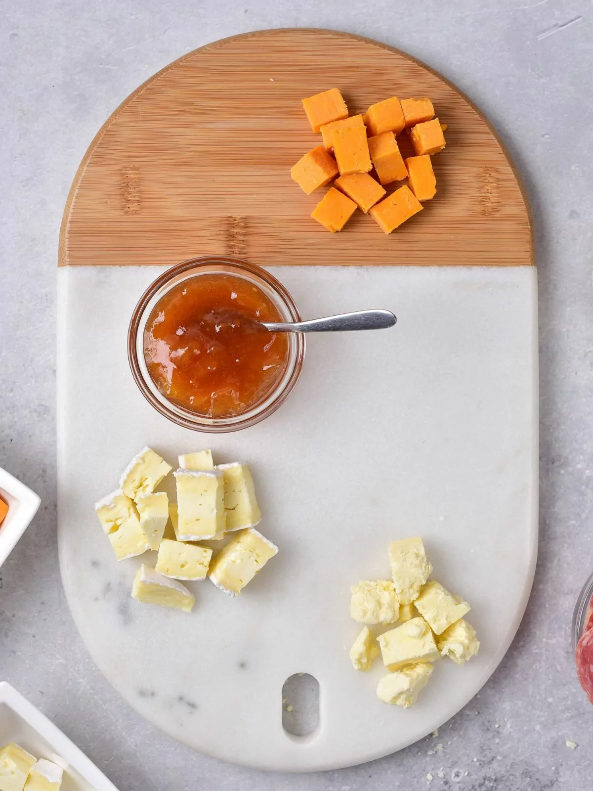 Different cheeses and chutney on cutting board.