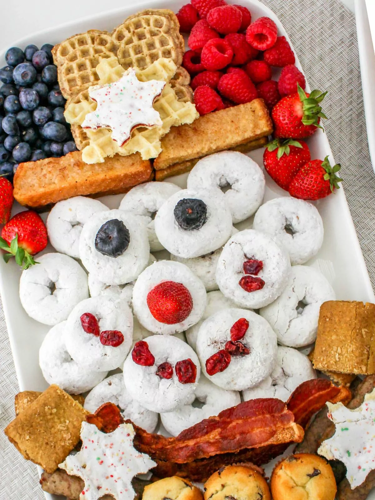 Snowman board with muffins, fruit, donuts, bacon.
