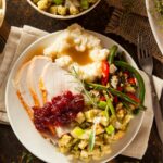 turkey dinner with stuffing, mashed potatoes, green beans and cranberry sauce on plate.