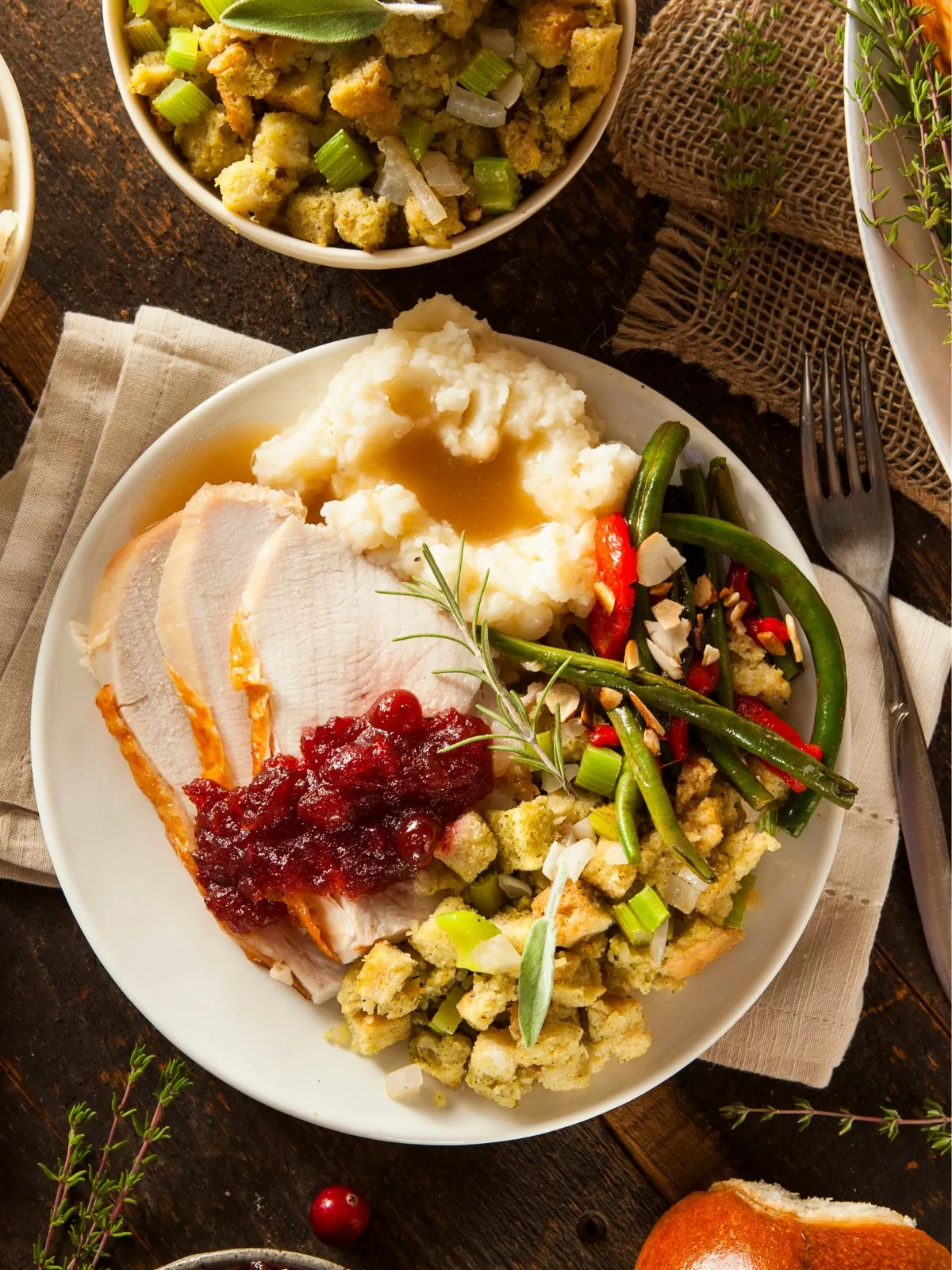 turkey dinner with stuffing, mashed potatoes, green beans and cranberry sauce on plate.