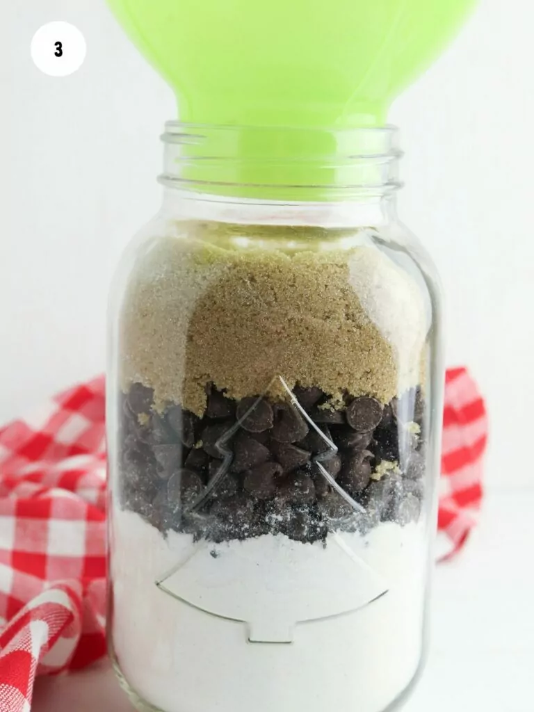 brown sugar on top of chocolate chips in mason jar with green funnel.