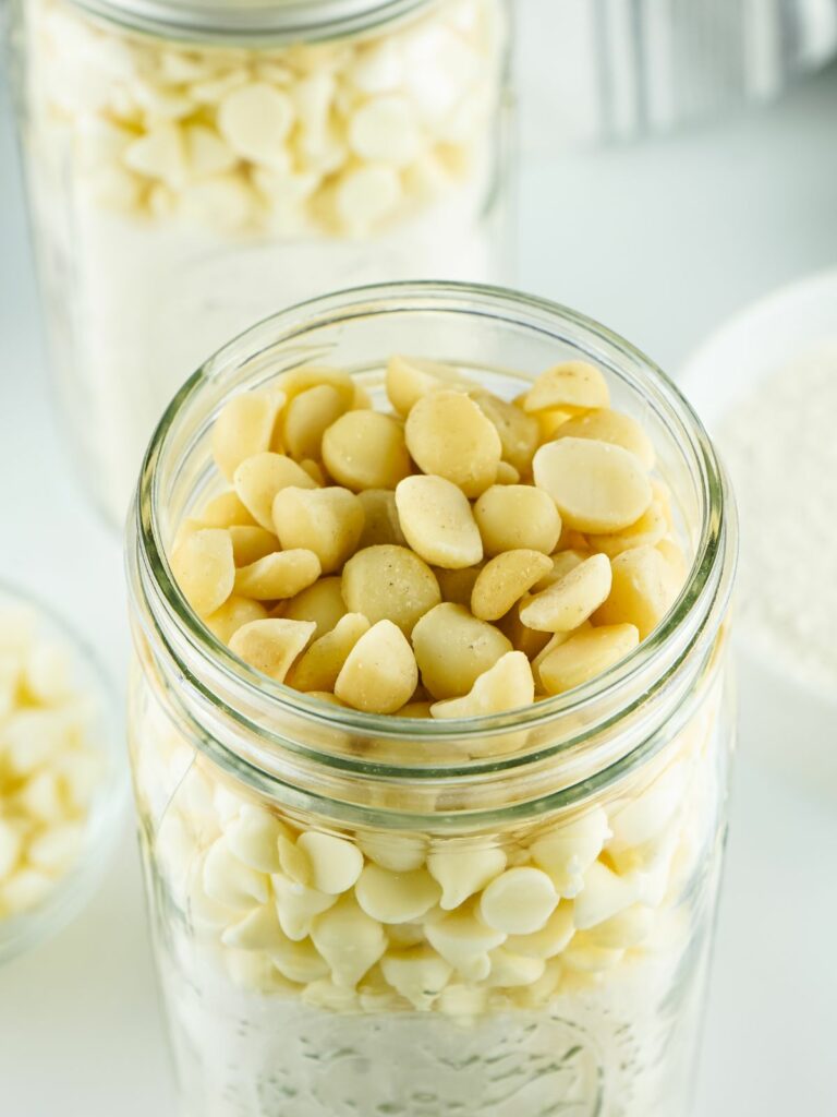 Add macadamia nuts on top of white chocolate chips in mason jar.
