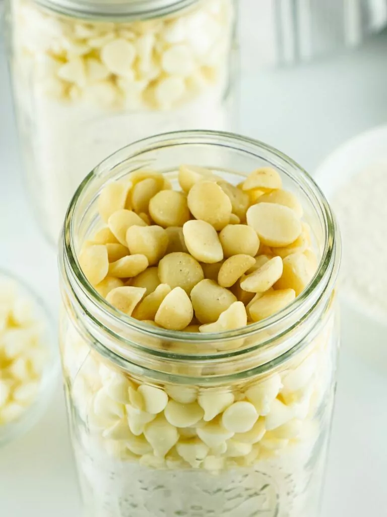 Add macadamia nuts on top of white chocolate chips in mason jar.