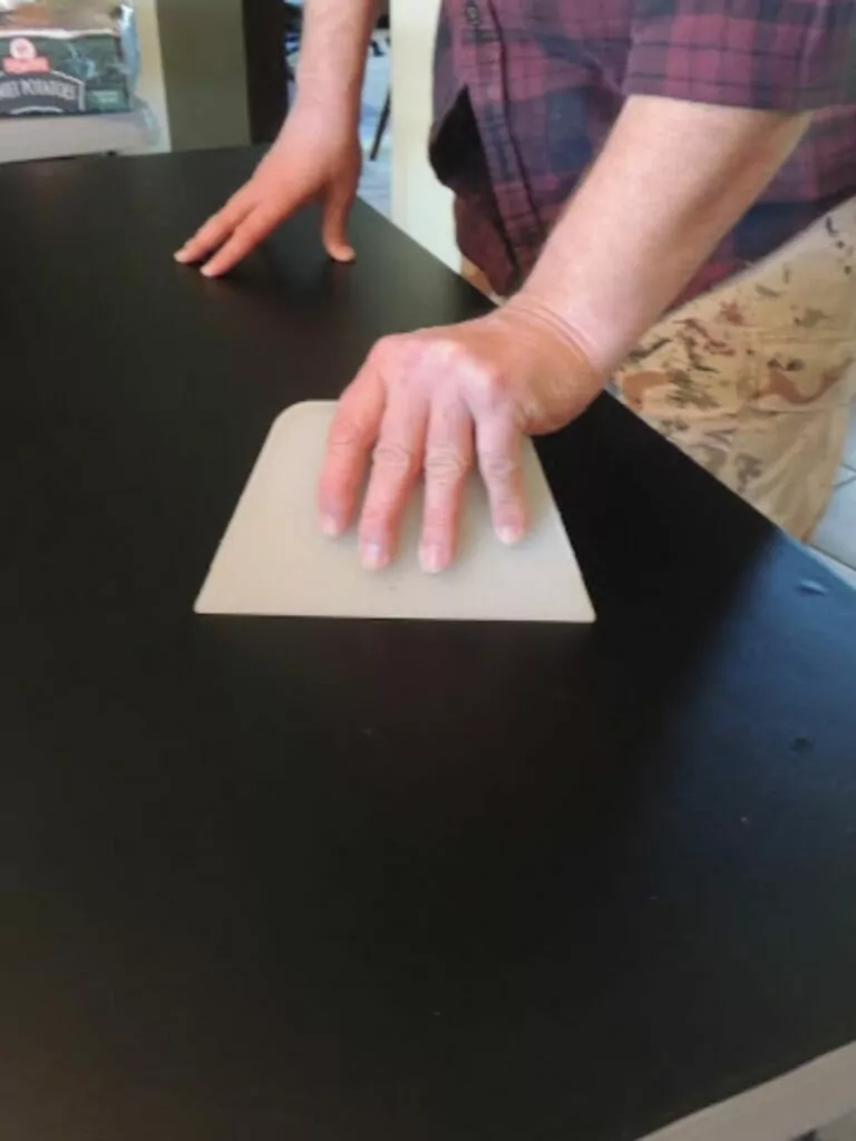Using a wallpaper scraper to adhere chalkboard vinyl to table.