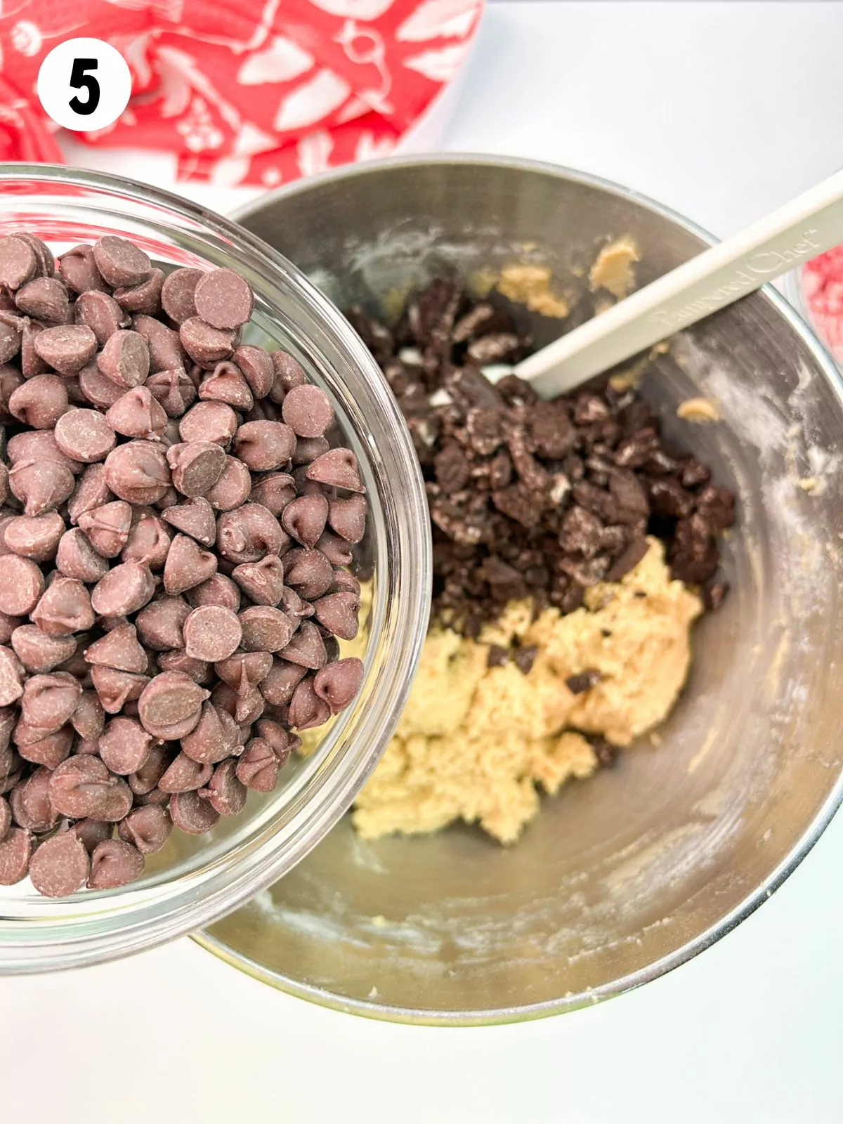 chocolate chips in small bowl being held over cookie dough batter.
