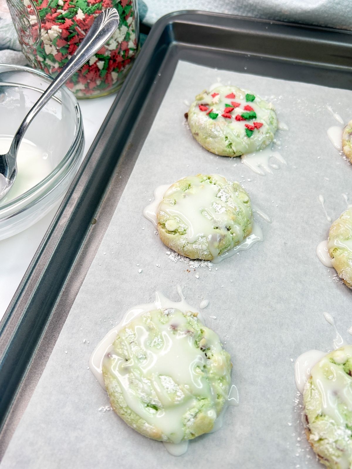 Powdered sugar glaze drizzled on top of cookies on baking sheet.