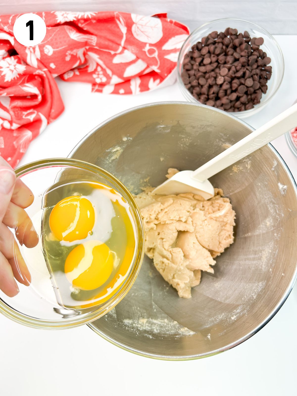 eggs in small bowl being held over cookie dough batter.