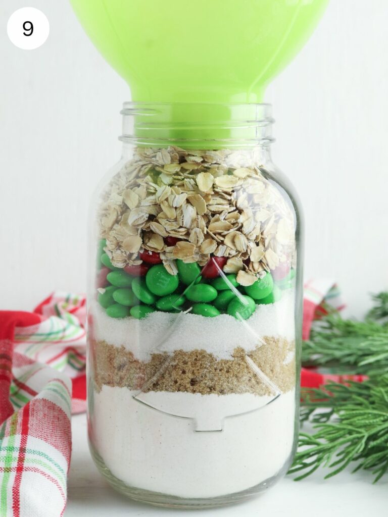 ingredients for oatmeal cookies in mason jar with green funnel.