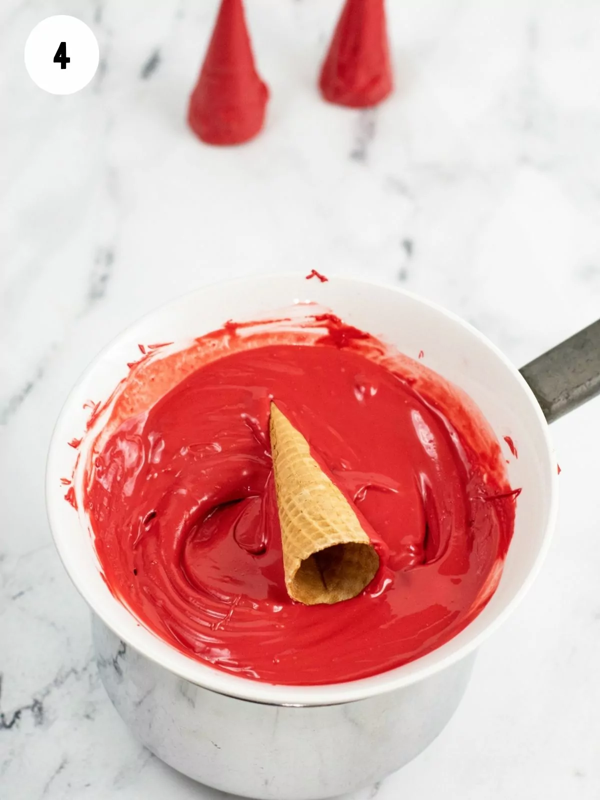 Ice cream cone being dipped in melted red candy pieces.