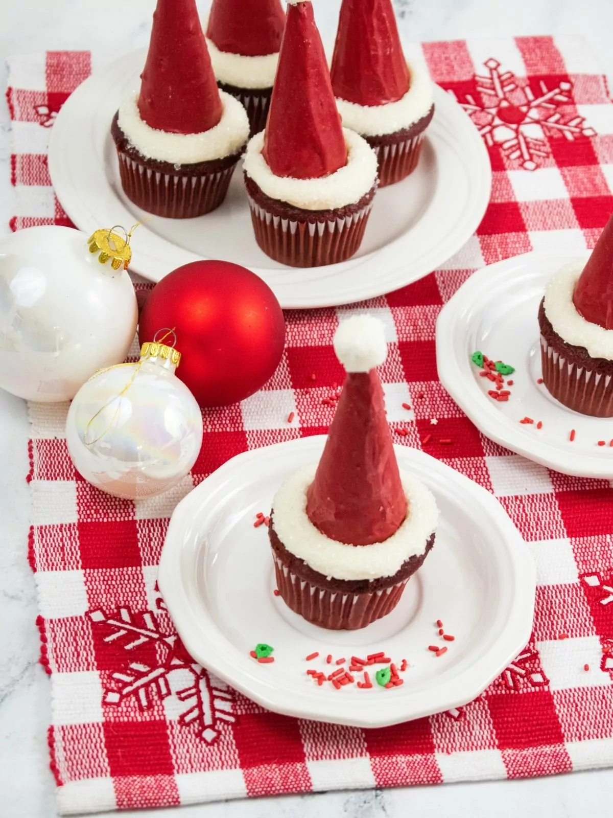 Santa hat cupcakes decorated with Christmas decorations in background.