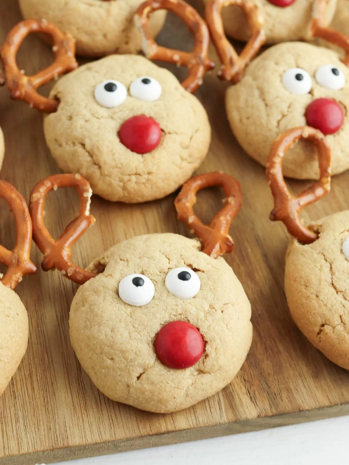 Peanut butter cookies decorated as reindeer on cutting board.