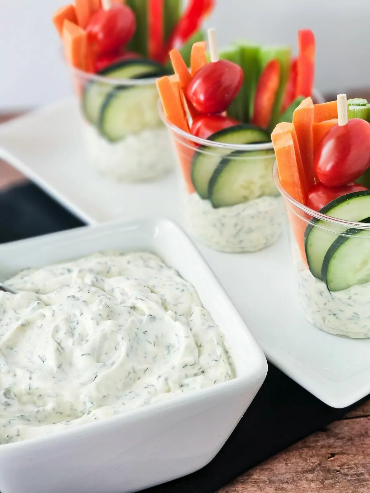 Dill dip in bowl with cups filled with dip and veggies.
