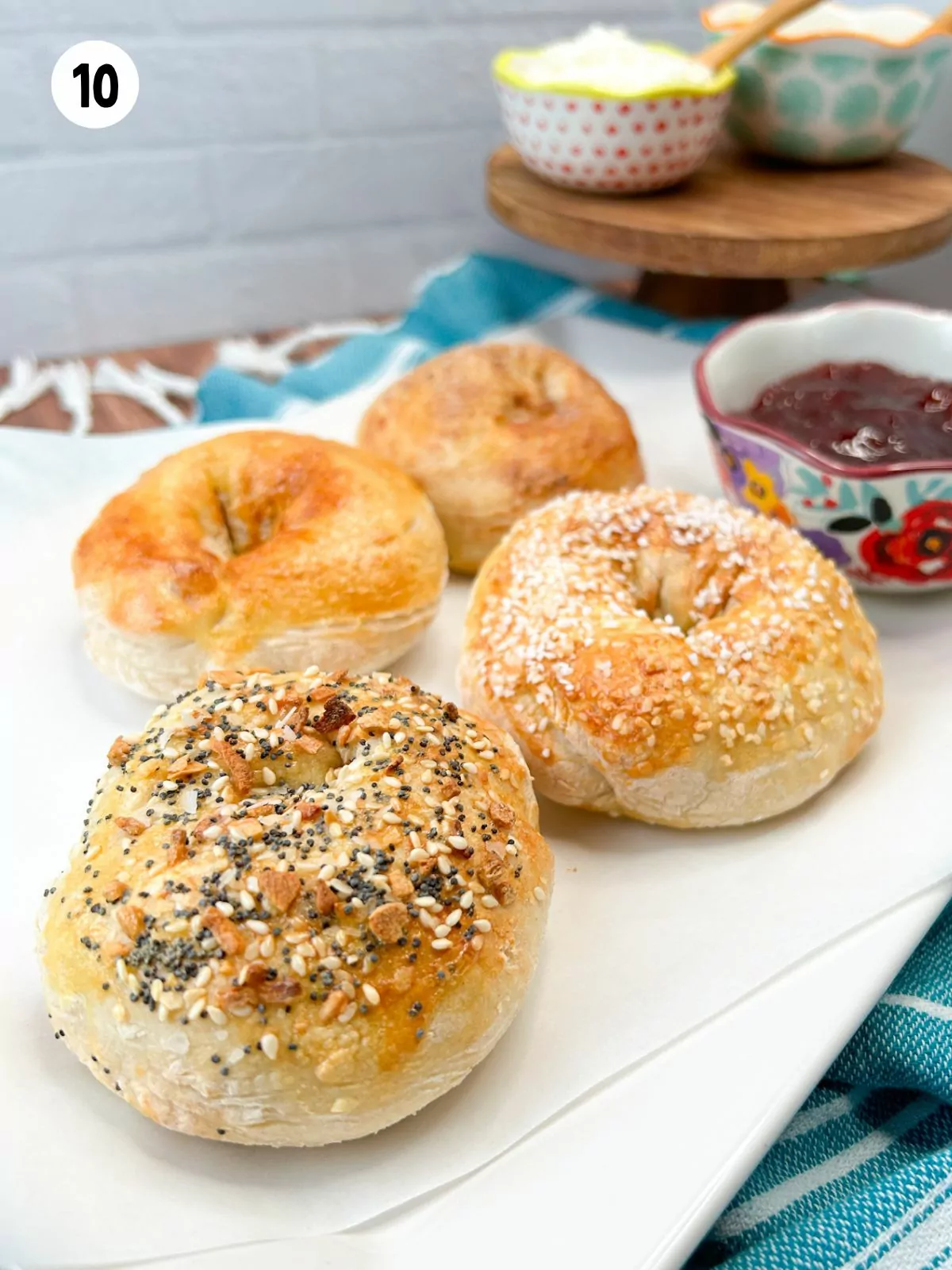 4 bagels on serving tray with jam, butter and cream cheese in small bowls.