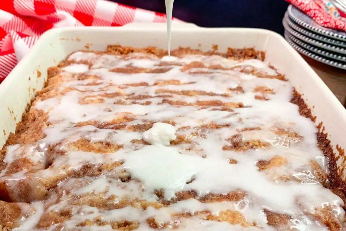 A cinnamon roll cake with icing being drizzled on top.