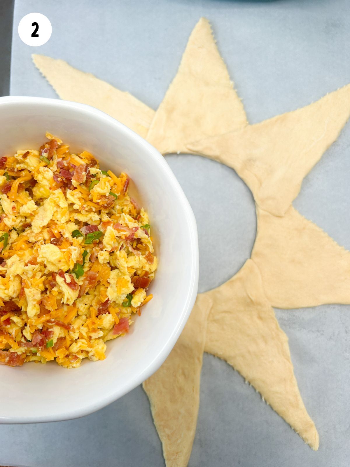 cooked scrambled eggs in white bowl with crescent roll triangles on baking sheet.