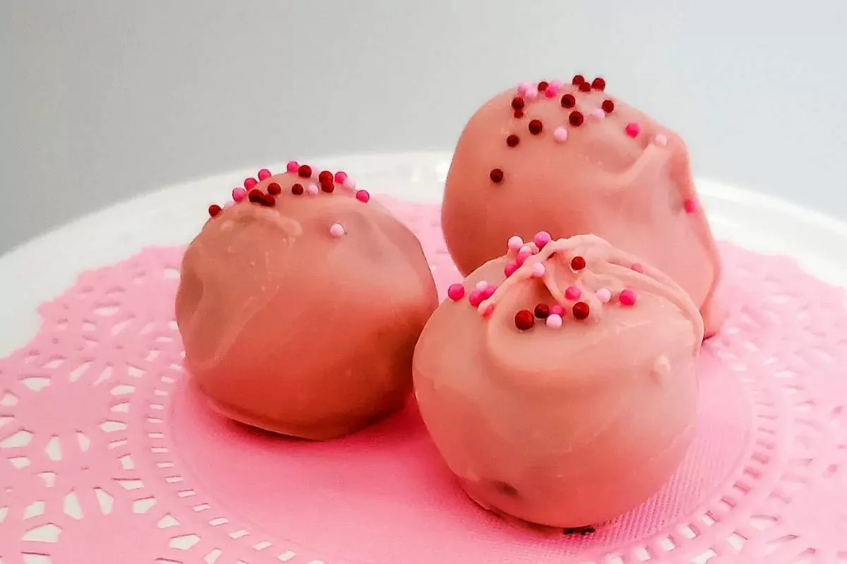 Three pink chocolate truffles with sprinkles on a pink plate.