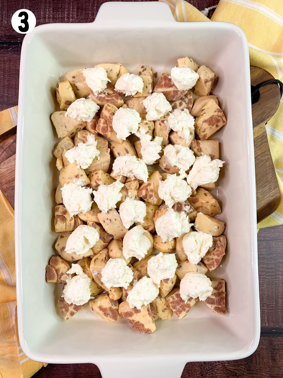 dollops of cream cheese on top of cut up cinnamon rolls in casserole dish.