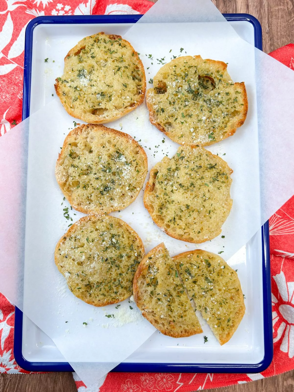 English muffins toasted with homemade garlic butter on white tray and red flowered dish towel.